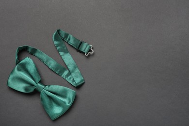 Stylish green satin bow tie on dark background, top view. Space for text