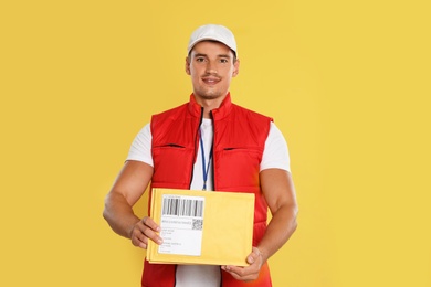 Happy young courier with envelopes on yellow background