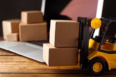 Toy forklift with boxes near laptop on wooden table. Logistics and wholesale concept