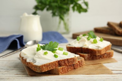 Bread with cream cheese, green onion and parsley on white wooden table