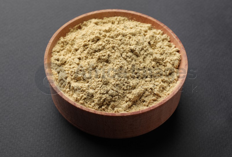 Photo of Aromatic ginger powder in wooden bowl on dark background