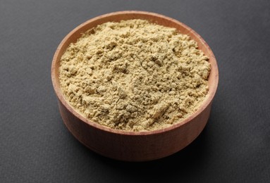 Aromatic ginger powder in wooden bowl on dark background