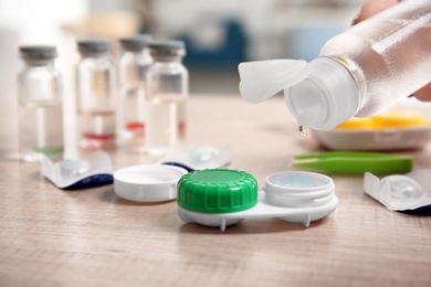 Woman dripping solution into contact lens case on table, closeup