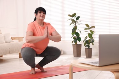 Overweight mature woman practicing yoga at home, space for text