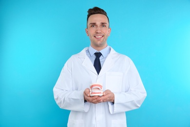 Male dentist holding jaws model on color background