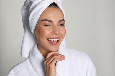 Beautiful young woman wearing bathrobe and towel on head against light background
