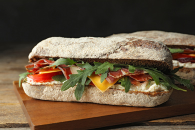 Photo of Delicious sandwich with fresh vegetables and prosciutto on wooden table, closeup