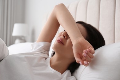 Young woman suffering from migraine in bed at home