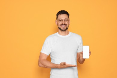 Happy man showing smartphone on orange background. Space for text