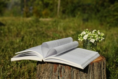 Photo of Open book and flowers on tree stump outdoors