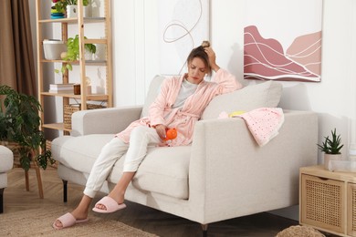 Tired young mother sitting on sofa in living room