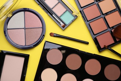 Photo of Different contouring palettes and brushes on yellow background, flat lay. Professional cosmetic product