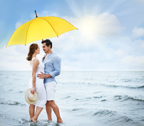 Image of Happy young couple with umbrella for sun protection on beach near sea