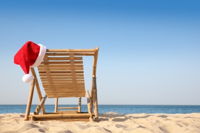 Photo of Sun lounger with Santa's hat on beach, space for text. Christmas vacation