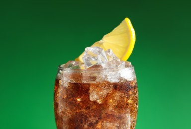 Glass of refreshing soda drink with ice cubes and lemon on green background, closeup