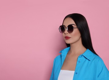 Attractive serious woman in fashionable sunglasses against pink background. Space for text