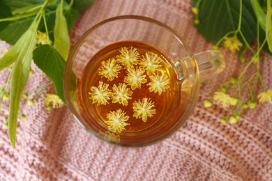 Glass cup of aromatic tea with linden blossoms on pink cloth, flat lay