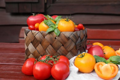 Different sorts of tomatoes with basil on wooden table