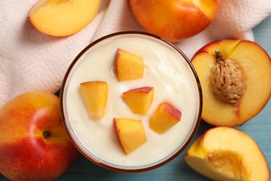 Tasty peach yogurt with pieces of fruit in glass on light blue wooden table, flat lay