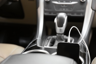 Photo of Mobile phone with charging cable in car, closeup