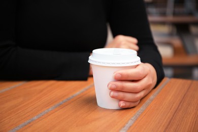Photo of Woman with cardboard cup of coffee at table, closeup