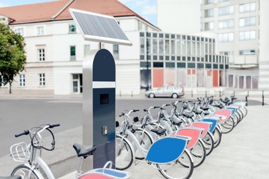 Station with solar panel and many bicycles on city street. Bike rental fleet