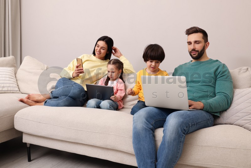 Photo of Happy family with gadgets on sofa in living room