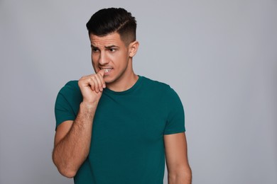 Photo of Man biting his nails on grey background, space for text. Bad habit