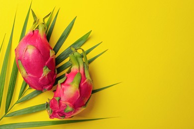 Photo of Delicious pitahaya fruits with palm leaf on yellow background, flat lay. Space for text