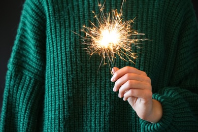 Woman in green sweater holding burning sparklers, closeup