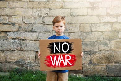 Sad boy holding poster with words No War against brick wall outdoors