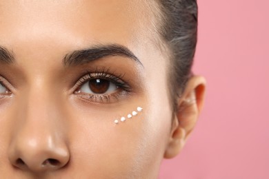Woman with cream around eye on pink background, closeup. Skin care