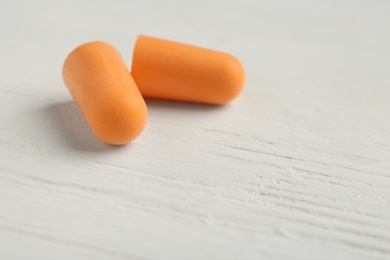 Pair of orange ear plugs on white wooden background, closeup. Space for text