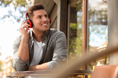 Handsome man with headphones listening to music in outdoor cafe, space for text