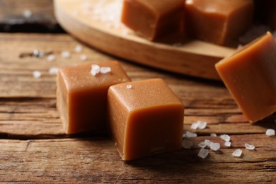 Photo of Yummy caramel candies and sea salt on wooden table, closeup