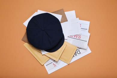 Postman hat, newspapers and mails on light brown background, flat lay