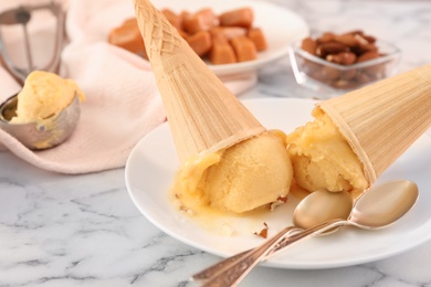 Plate with delicious yellow ice cream in wafer cones and spoons on white marble table, closeup