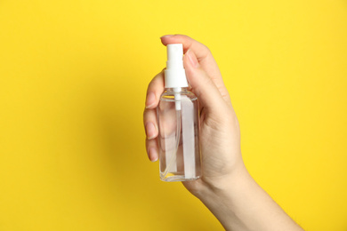 Photo of Woman holding antiseptic spray on yellow background, closeup