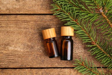 Bottles of pine essential oil and conifer tree branches on wooden table, flat lay. Space for text