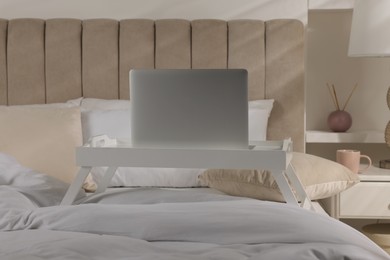 White tray table with laptop on bed indoors