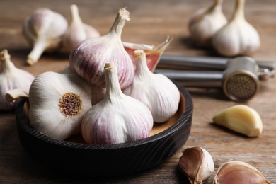 Fresh organic garlic in bowl on wooden table, closeup