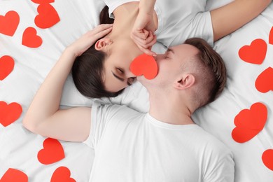 Photo of Lovely couple kissing behind decorative heart on bed, top view. Valentine's day celebration