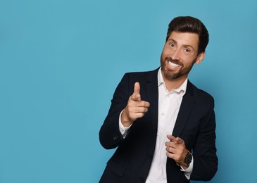 Photo of Smiling bearded man pointing forward index fingers on light blue background. Space for text