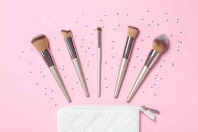 Photo of Bag and different makeup brushes on pink background, flat lay