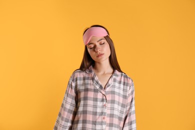 Young woman wearing pajamas and mask in sleepwalking state on yellow background