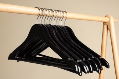 Black clothes hangers on wooden rack against beige background, closeup view