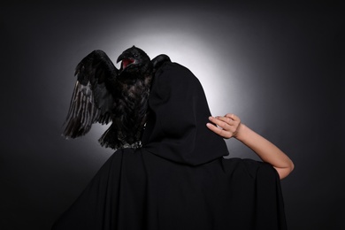 Mysterious witch with raven on black background, back view