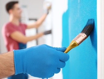 Male decorator painting wall with brush indoors, closeup