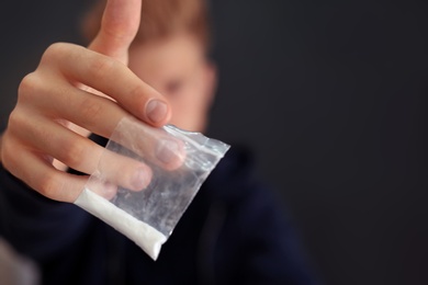Criminal holding plastic bag with drug against dark background, space for text