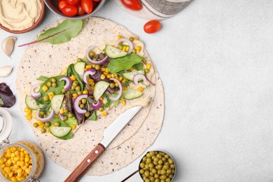 Photo of Tortilla with hummus and vegetables on light table, flat lay. Space for text